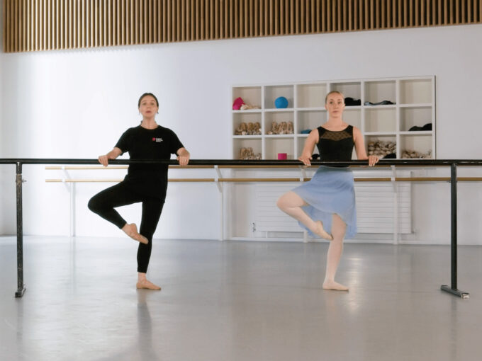A ballet teacher and a demonstrator in a retiré position at the barre