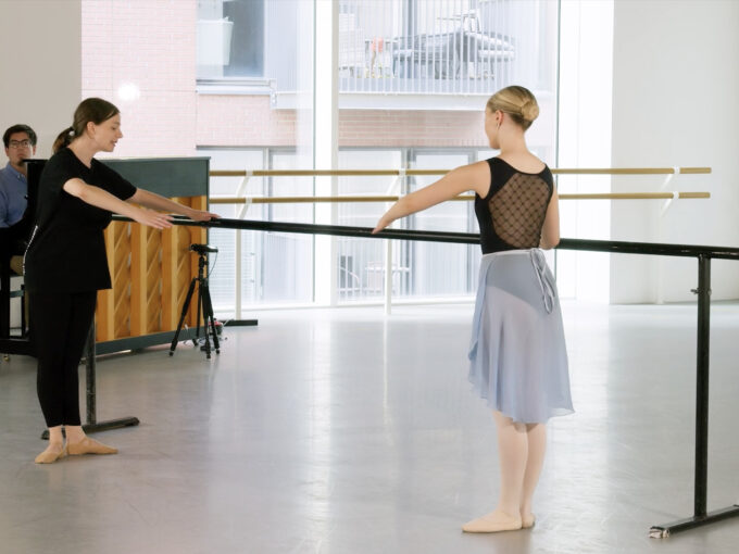A ballet tutor and a demonstrator doing a port de bra at the barre