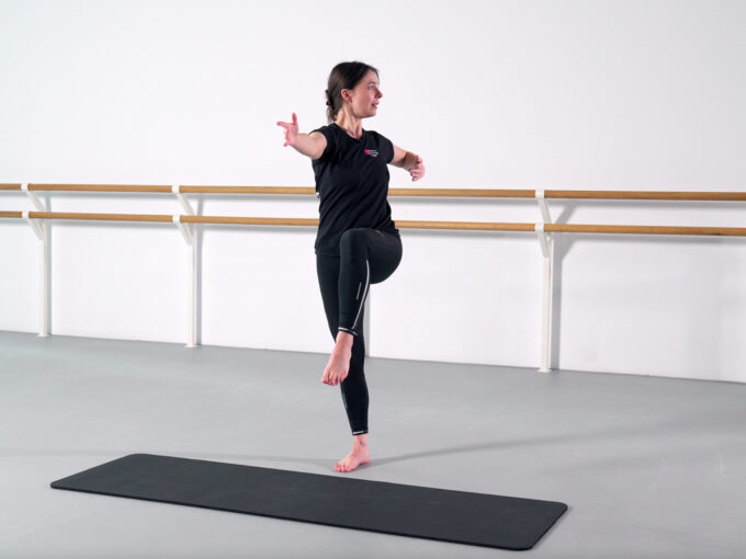 A dance demonstrator does a standing stretch in the centre next to a mat