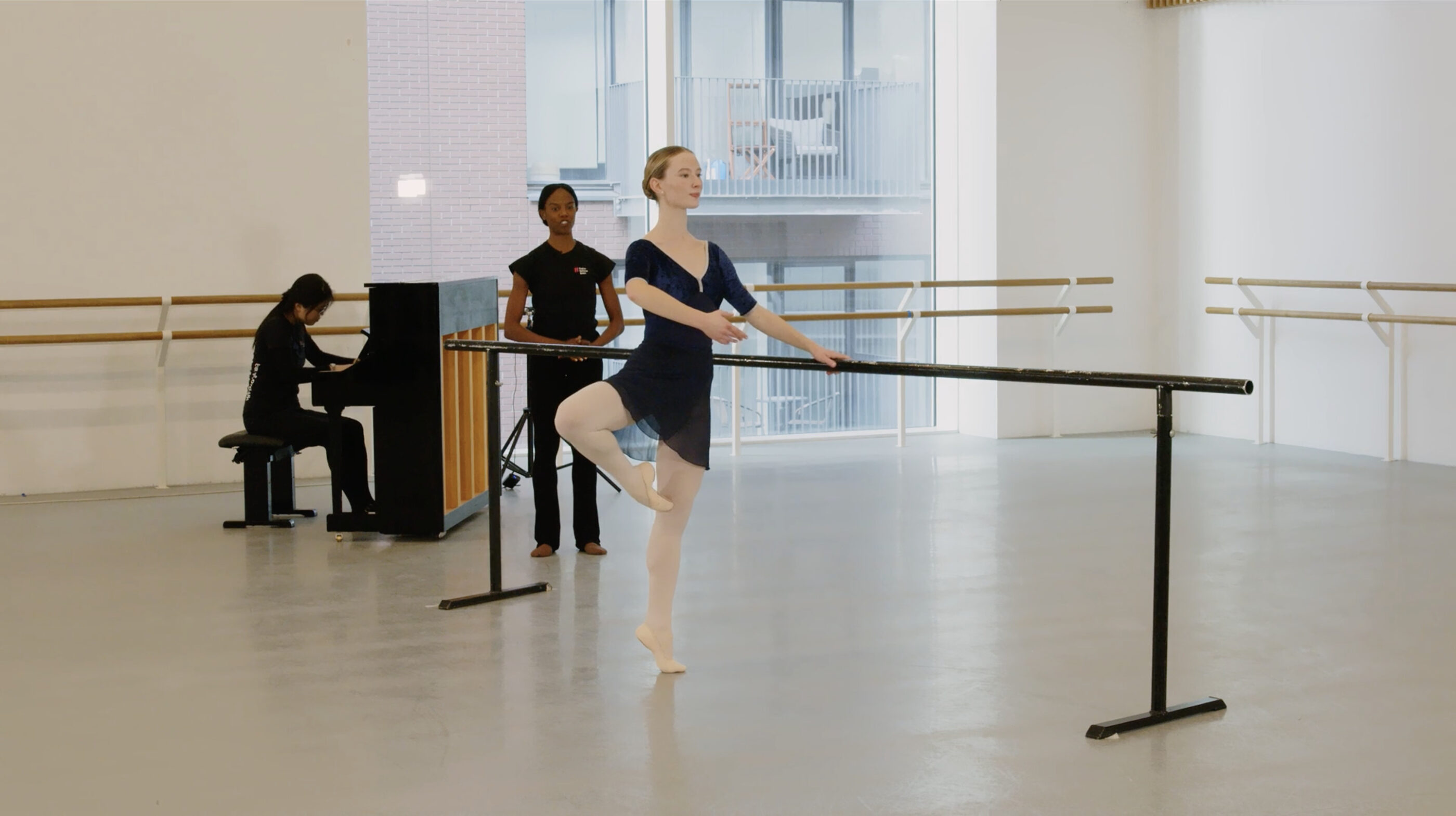 A ballet demonstrator is standing in retire position at the barre.