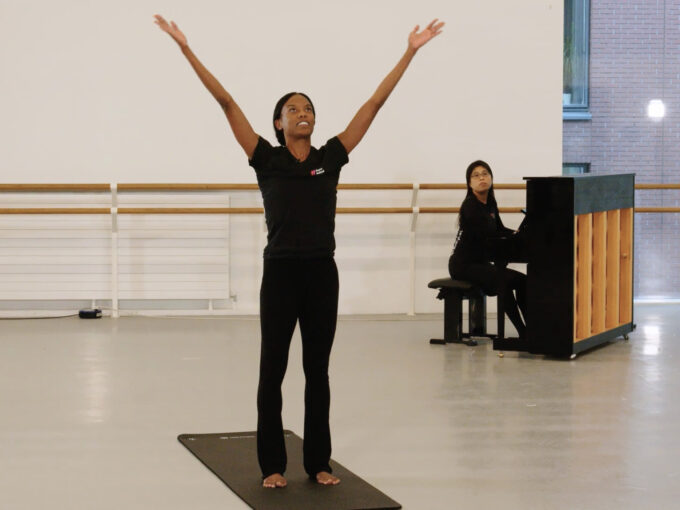 A woman in black attire stands on a yoga mat, her arms lifted towards the ceiling